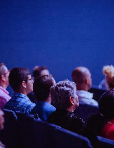 An attentive group of adults seated at an indoor conference, focusing on a presentation.