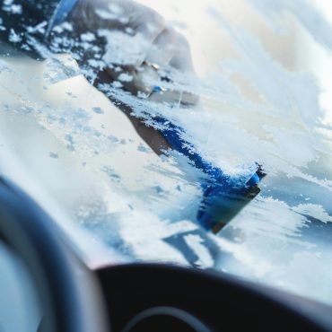 Hand scraping ice off a car windshield during a cold winter morning.