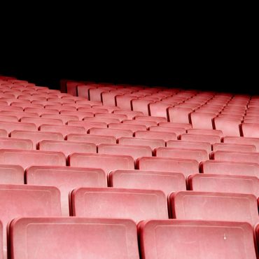 Rows of red seats in an empty auditorium with dramatic lighting.